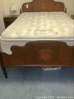 Full view of assembled double bed with mattress showing wooden headboard and footboard with carved inlay and tufted mattress surface