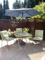 Full view of the patio set including four chairs with striped cushions, table with glass top and umbrella opened above it.