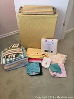All items shown: vintage woven hamper, pile of assorted towels, bedding linens including packaged full-size set, and small cloths.