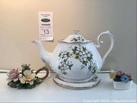 Front view of Royal Albert teapot with floral design and accompanying porcelain flowers on either side