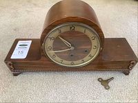 Full view of vintage wooden mantle clock on beige carpet surface with one winding key visible in front.