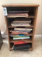 Front view of the wooden storage cabinet filled with vintage sheet music and music books across multiple shelves.