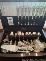Full view of open flatware case displaying knives, forks, spoons, and serving utensils all with ornate handles
