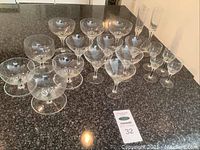View of most of the crystal glassware arranged on dark countertop showing the clear starburst cut design on the rounded bowl glasses, including coupes and flutes.