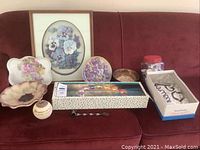 Full lot displayed on couch including floral plates, framed pansy art, candle holder, tea candles, and additional items