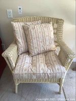 Front view of the wicker chair with seat and back cushions attached, placed on carpeted floor.