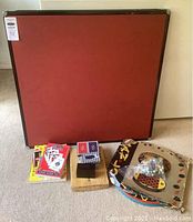 Photo of red felt card table with wood frame, assorted playing cards, and boxed games scattered around its base.