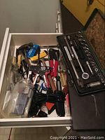 Drawer containing assorted hand tools including pliers, hammer, staple tool, and other small tools.