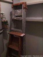 Photo showing the 6' aluminum ladder folded and leaning against the wall in a storage or utility area, with the 4' wooden step ladder in front of it.