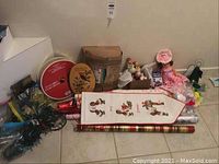 Photo showing assortment of Christmas lights, gift wrap rolls, wall hanging, ribbons, and vintage toys including a rag doll.