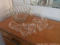 Clear glass punch bowl and twelve cups on wooden surface, one cup differs in appearance.