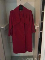 Front view of the red velvet-like coat hanging on a hanger showing full length and shape.
