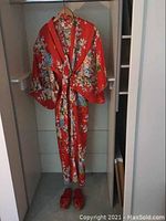Full view of red floral kimono hanging with matching red floral slippers on the floor beneath, showing overall shape and pattern.