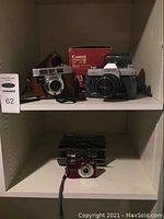 Shelf view showing three cameras including Canon FTb with box and Kodak 35mm camera, and Nikon digital camera below