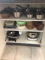 Full cupboard view showing amber glass casserole dishes, green glass bake dish, brown ceramic casseroles, stacks of metal pans and white plastic containers.