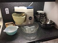 Kenwood Chef stand mixer with yellow mixing bowl attached, surrounded by additional mixing bowls of glass and metal on kitchen counter.