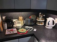 Overview of kitchen counter showing Sunbeam electric kettle, stainless steel Sunbeam toaster, Black & Decker coffee maker, Oskar electric chopper, Kitchen Works electric can opener, spice rack and accessories