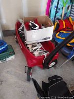 Overall view of red Radio Flyer wagon filled with ice skates in various sizes and a cardboard box.