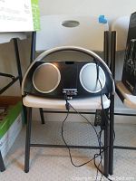 Front view of Harman Kardon speaker system with two silver speaker grills, power adapter, and remote control on a folding chair.