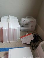 Full view of white Singer sewing machine with manual, foot pedal, and carrying case