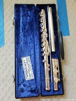 Full view of silver-colored Arduini flute disassembled into three parts arranged in blue velvet-lined black hard case.