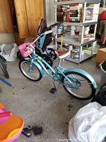 Full side view of blue Trek bicycle with pink front basket, brown and white padded saddle, and black pedals.