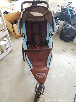 Front view of brown and blue Baby Jogger Revolution BoB jogger stroller showing seat, harness, and front wheel.