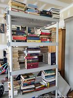 Four shelves holding varying stacks of books in mixed conditions, showing titles and spines.