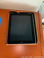 Front view of iPad showing black screen and carrying case underneath with orange trim visible.