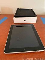 Front view of Apple iPad on wooden surface with black case and white Apple box behind