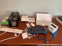 Full view showing all items on table including Apple keyboard, mouse, Magic Trackpad, Apple TV box, Wemo switch, surge protectors and cables