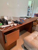 Full view of the wooden rectangular desk with items on top and a chair next to it.