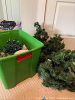 Plastic bin with artificial Christmas greenery branches adjacent to more greenery on carpet.