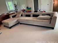 Full view of two piece beige sectional couch showing overall shape, design, and condition with visible wear and fabric tears.