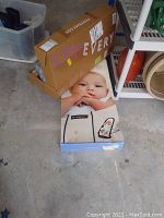 Boxes of BabyBjorn Babysitter Balance and Lovevery Baby Play Gym items, placed on a concrete floor alongside storage shelving.