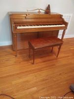 Full view of Wurlitzer upright piano with bench in wooden finish on hardwood floor
