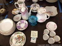 Top-down photo showing a variety of china, including a floral pitcher, multi-colored floral plates, small cups, and a blue glass jar in the center