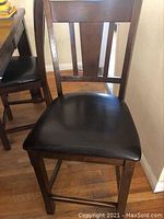 Close-up of a dark wood dining chair with black cushioned seat, showing wood finish and upholstery condition.