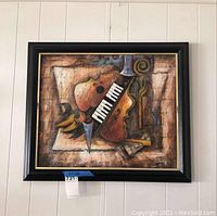 Framed wall art painting showing signed abstract composition of violin, piano keys, and trumpet on textured canvas.