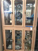 Front view of wood and glass curio cabinet with three doors on top and two doors on bottom, containing various ceramic dishware.