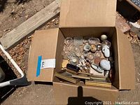 Box containing various small vintage glass and porcelain decorative items including candle holders, small dishes, figurines, and framed pictures.