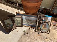 Full view of vintage artwork pieces arranged on ground near clay pot, includes varied sizes and frames