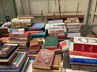 Wide view of assorted books stacked on a table showing different sizes, colors, and condition including vintage and new editions.