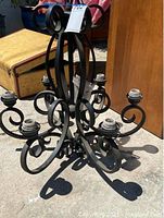 Black iron candelabra style hanging lamp shown from angle top-down, displaying six arms with sockets for bulbs, black wrought iron with ornamental scroll design.