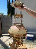 Chandelier held by hand showing pink frosted glass shade with floral decoration and gold metal trim with attached crystal prisms.