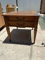 Front view of the vintage wood end table showing drawer and tapered legs with decorative handles.