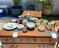All items arranged on a wooden surface including cups, pots, dishes, and decorative boxes shown together