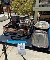 Wide view of various silver plated serving pieces on a table including trays, tea set, and condiment holders.