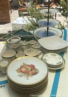 Full view of assorted holiday serving dishes showing ceramic plates with fruit motifs, small cups, square plates, and Christmas tree shaped plates.