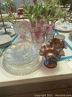 Image showing assorted clear patterned plates, purple tinted glasses, and ruffled edge bowls on table.